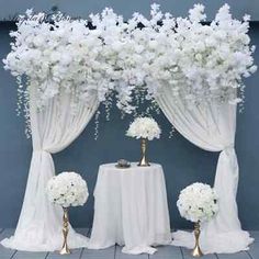 white flowers and gold vases sit on a table with drapes in the background