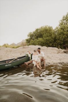 a man and woman sitting in the water next to a canoe