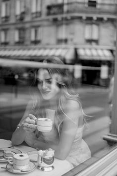 a woman sitting at a table in front of a window with a cup of coffee