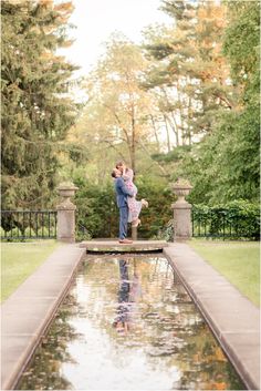 an engaged couple standing in front of a pond with their arms around each other and kissing