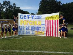 some cheerleaders are standing in front of a sign that says get your popcorn we're about 2 put on a story