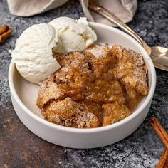 two scoops of ice cream in a bowl next to cinnamon sticks and an apple cobbler