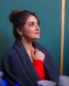 a woman with her hair in a bun wearing a red sweater and hoop earrings looking off into the distance