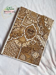 a brown and white patterned notebook sitting on top of a bed next to a pen