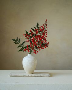 a white vase filled with red berries on top of a table