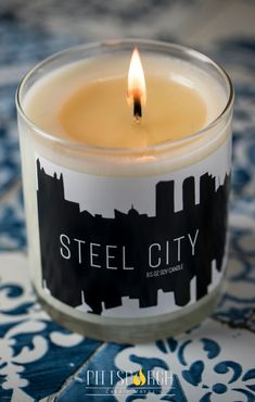 a candle that is sitting on top of a blue and white table cloth with the words steel city printed on it