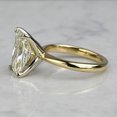 a yellow gold engagement ring with a pear shaped diamond in the center on a marble surface