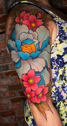 a woman with a colorful flower tattoo on her arm and shoulder is standing in front of a brick wall