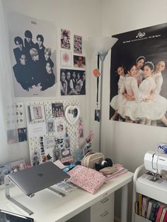 a white desk topped with a laptop computer sitting next to a wall covered in pictures