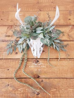 a deer's head is adorned with greenery and flowers on a wooden surface