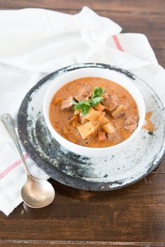 a white bowl filled with soup on top of a wooden table next to a spoon