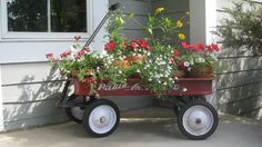 a red wagon filled with potted flowers sitting on the side of a house next to a window