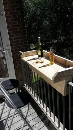 a wooden table with two bottles on top of it next to a metal chair and railing