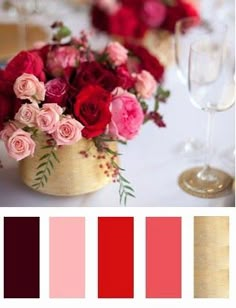 red and pink flowers in a wooden vase on a table with wine glasses, napkins and plates