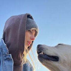 a woman in a hoodie is petting a dog's nose with her mouth