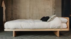 a bed with white sheets and pillows in a room next to a wooden flooring