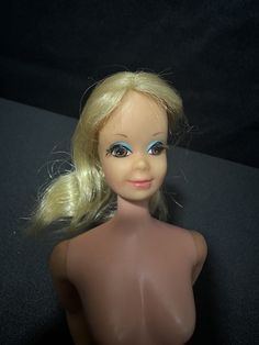 a doll with blonde hair and blue eyes is posed on a black surface in front of a dark background