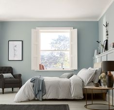 a bedroom with light blue walls and white trim on the windowsill, bed in foreground