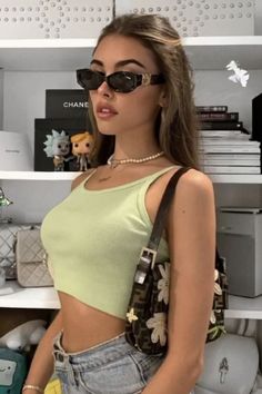 a woman wearing sunglasses standing in front of a shelf with books and purses on it