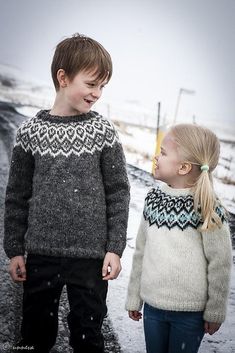 two young children standing next to each other on a snow covered road in the middle of winter