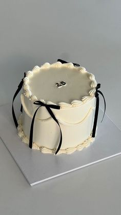 a white cake sitting on top of a silver plate with black ribbon around it's edge