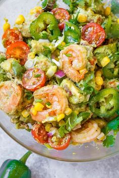 a glass bowl filled with shrimp, corn and tomato salad on top of a table