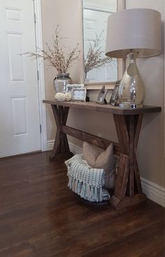 a wooden table topped with a lamp next to a mirror and vase filled with flowers