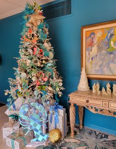 a decorated christmas tree sitting next to a table with presents on it in front of a blue wall