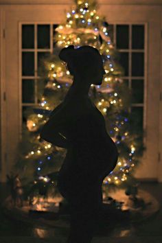 a lit up christmas tree in the corner of a room with a teddy bear statue next to it