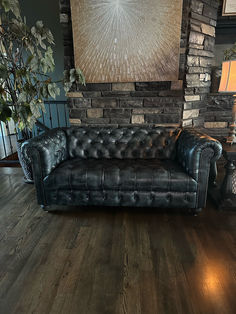 a black leather couch sitting in front of a brick wall with a painting on it