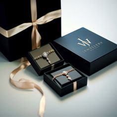 two black boxes with gold ribbons and rings in them next to a ribbon tied around the box