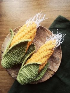 two crocheted corn cobs sitting on top of a wooden plate next to a green napkin