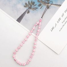 a pink and white beaded necklace next to an envelope with a palm tree in the background