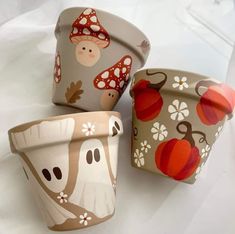 three pots with different designs on them sitting next to each other, one has mushrooms and the other has pumpkins