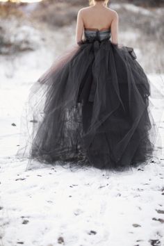 a woman in a black dress is standing in the snow with her back to the camera