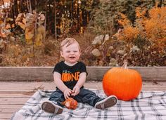 a toddler sitting on a blanket next to a pumpkin