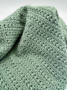 a green crocheted scarf laying on top of a white surface