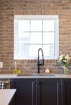 a kitchen sink sitting under a window next to a counter top with flowers on it