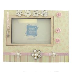 a pink and white photo frame with flowers on the front, decorated with buttons and ribbons