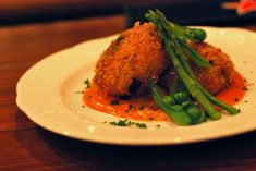 a white plate topped with meat covered in sauce and asparagus on a wooden table