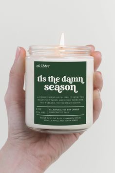 a hand holding a candle that says tis the damn, season in green and white