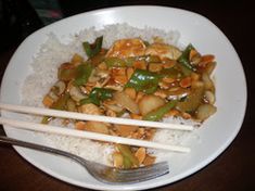 a white plate topped with rice covered in chicken and veggies next to chopsticks