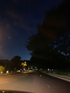 a car driving down a street at night time with the lights on and trees in the background