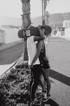 a man carrying a skateboard on his back while standing next to a woman in front of a palm tree