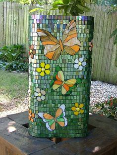 a vase made out of stained glass with butterflies and flowers on the outside, sitting on top of a wooden table