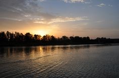 the sun is setting over water with trees in the background