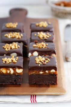 there are many pieces of chocolate cake on the cutting board with walnuts around it