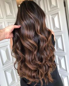 a woman with long, wavy hair standing in front of a door and holding her hand up to her head