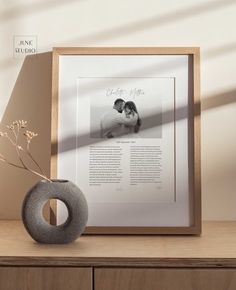 a vase with flowers in it sitting next to a framed photo on a table top