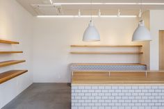 an empty room with wooden shelves and white tiled counter tops, along with hanging lights